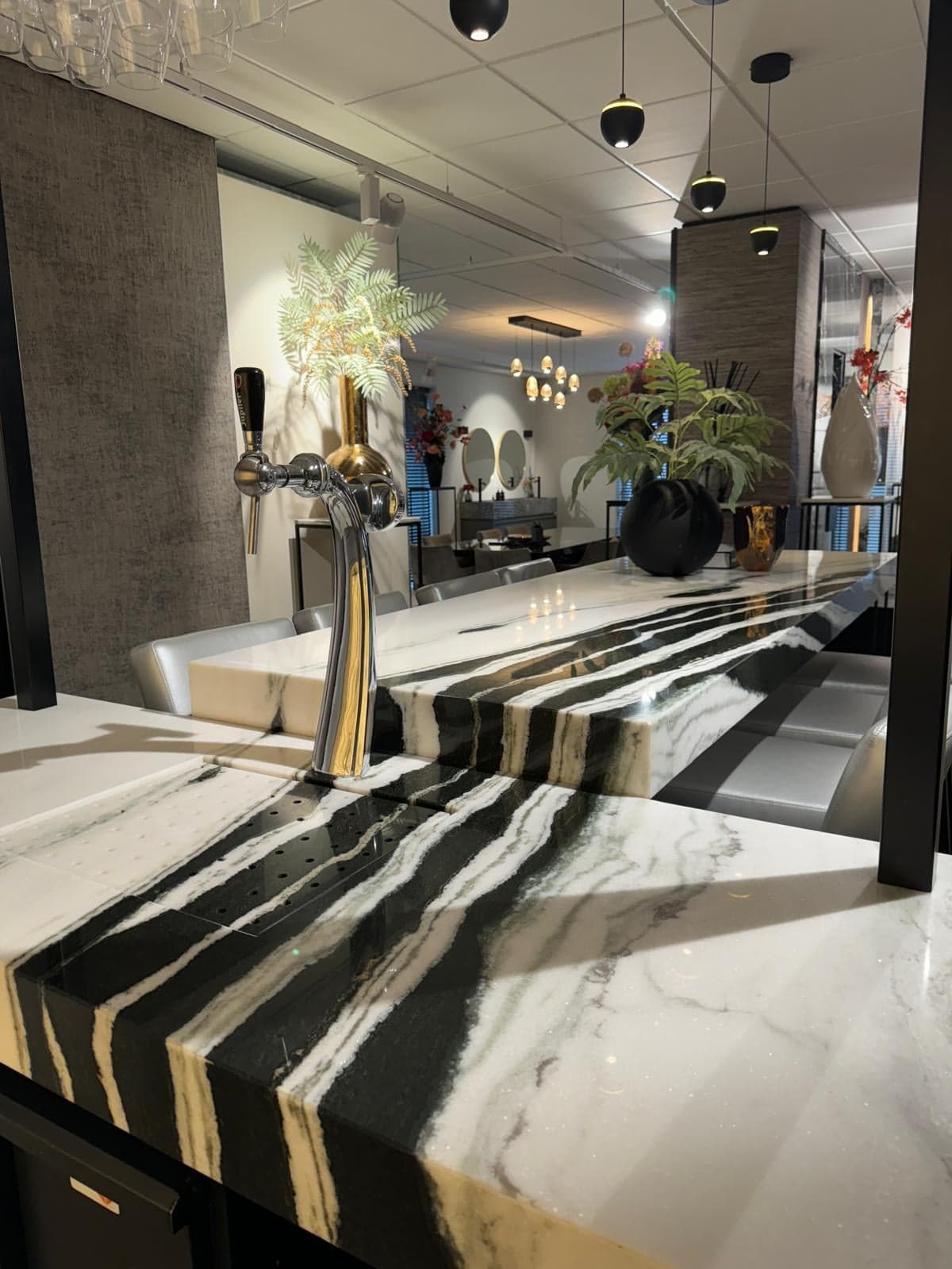 Bar met dramatisch geaderd zwart-wit natuursteen en een gouden tapkraan in een natuursteen-showroom in Tilburg