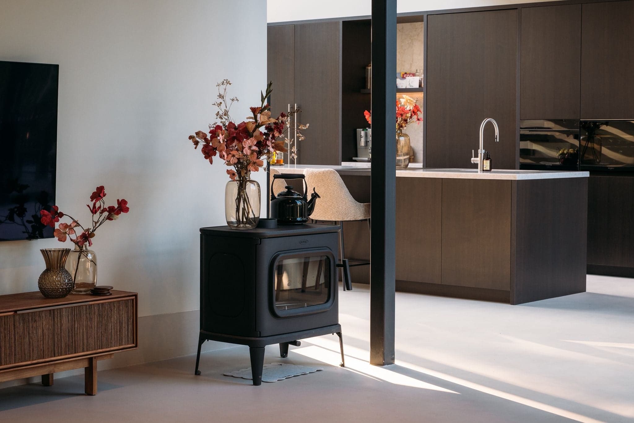 Zwarte houtkachel naast een houten dressoir met doorkijk naar de keuken in een villa in Sint-Oedenrode