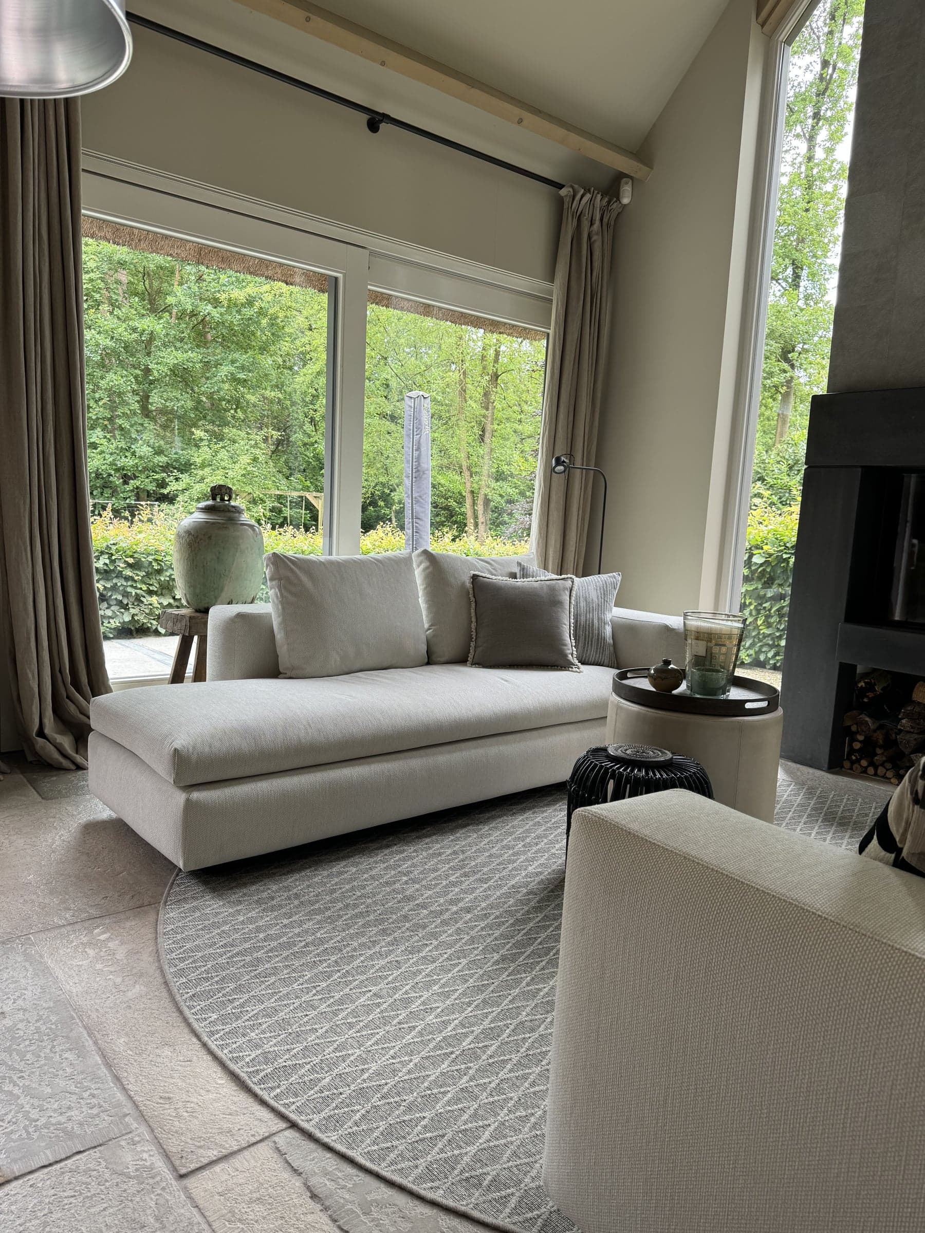 Woonkamer met witte loungebank en een grote raampartij met zicht op de groene tuin in een villa in Waalre