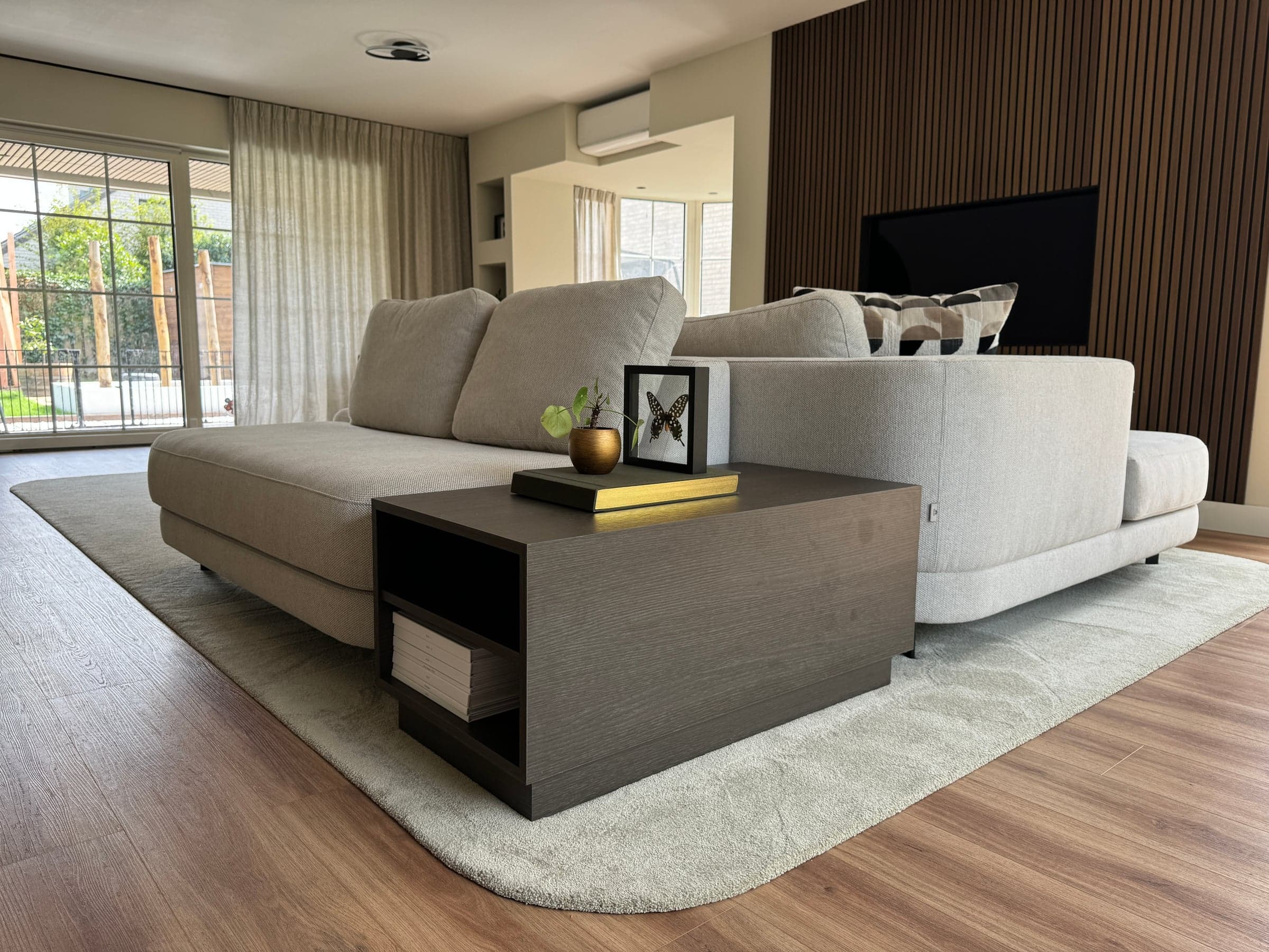 Woonkamer met grijze hoekbank en een donker eiken salontafel op een houten vloer in een woonhuis in Best