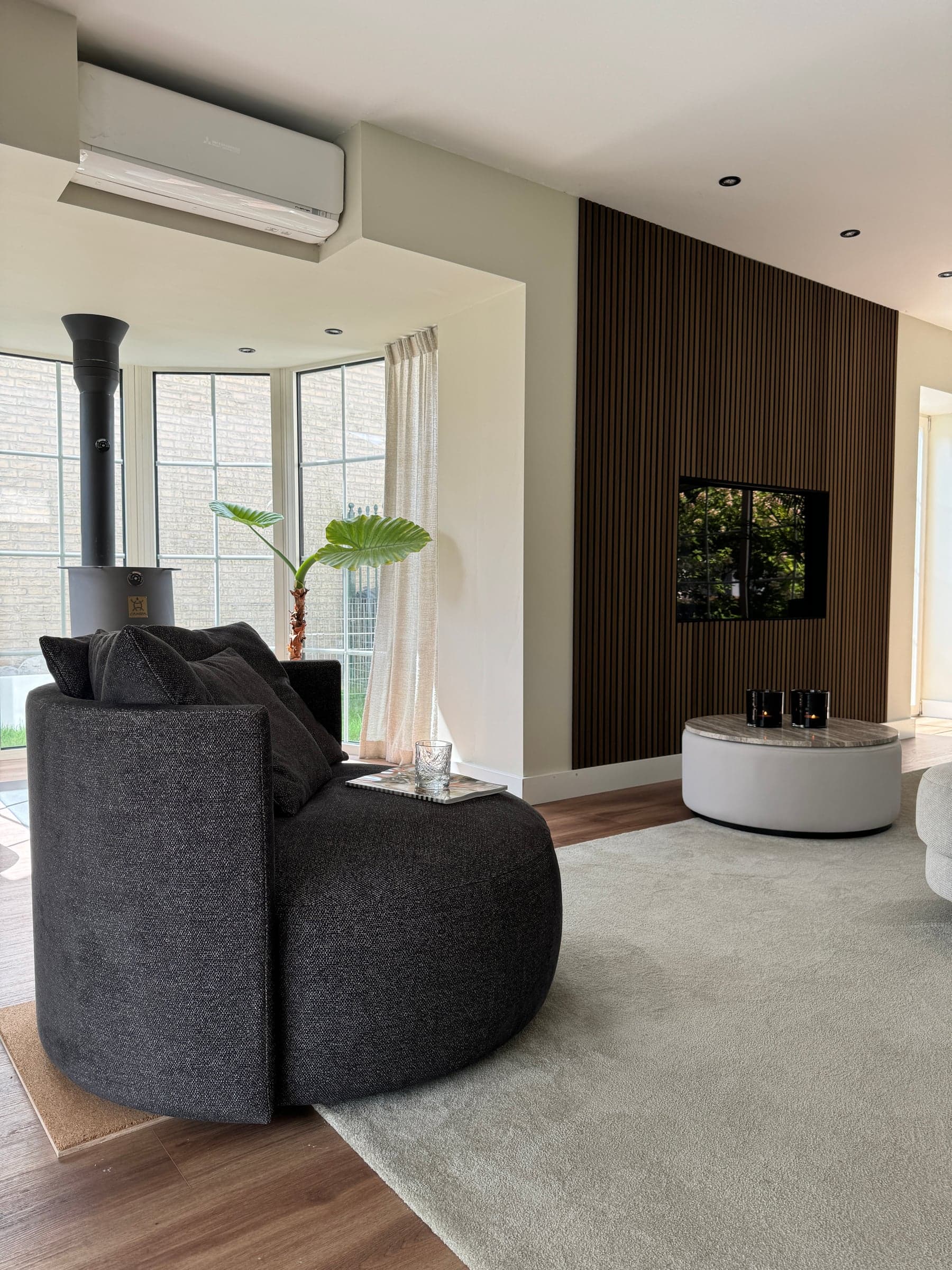 Woonkamer met een ronde antraciet loungestoel, houtkachel en houten lamellenwand in een woonhuis in Best