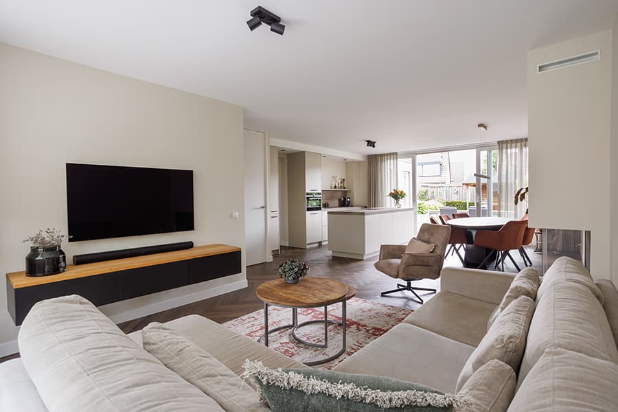 Woonkamer met zwevend tv-meubel, lichte bank en doorkijk naar de eetkamer en keuken in een woonhuis in Oisterwijk