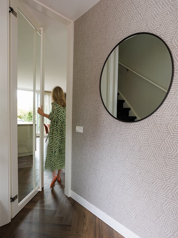 Hal met grafisch behang, ronde spiegel en visgraatvloer in een gerenoveerd woonhuis in Oisterwijk