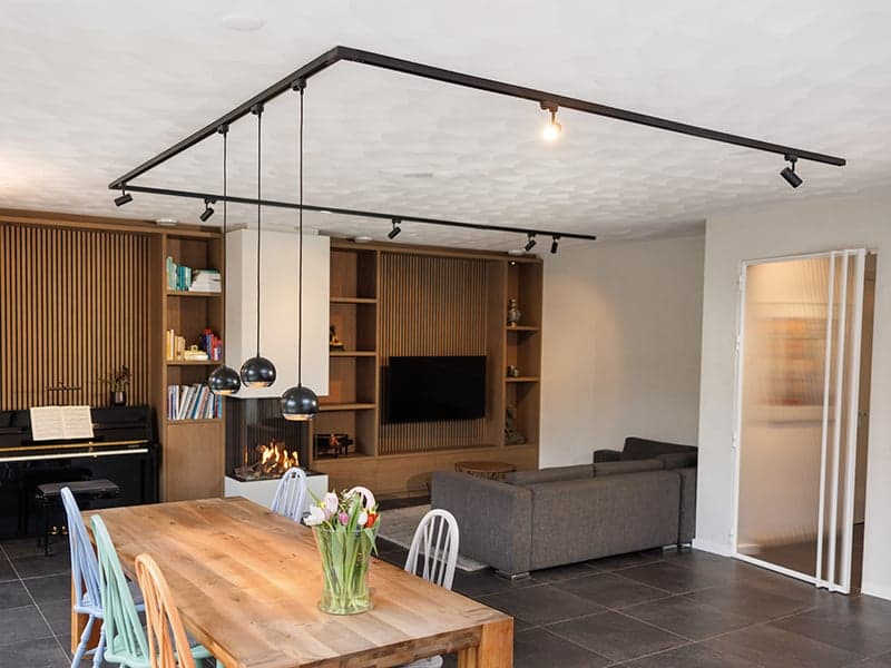 Eet- en woonkamer met een houten eettafel, railverlichting en een houten wandkast in een woonhuis in Oisterwijk