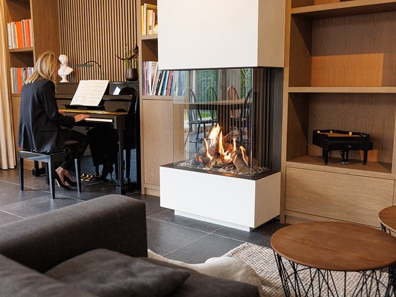 Zithoek met een driezijdige gashaard, houten boekenwand en een piano in een woonhuis in Oisterwijk