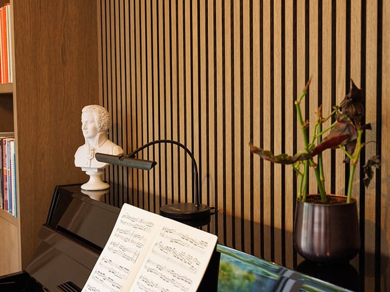 Pianodetail met bladmuziek en een buste tegen een houten lamellenwand in een woonhuis in Oisterwijk