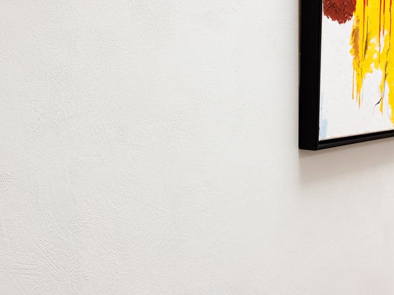 Wit gestuukte wand met een kleurrijk abstract schilderij in een zwarte lijst in een woonhuis in Oisterwijk