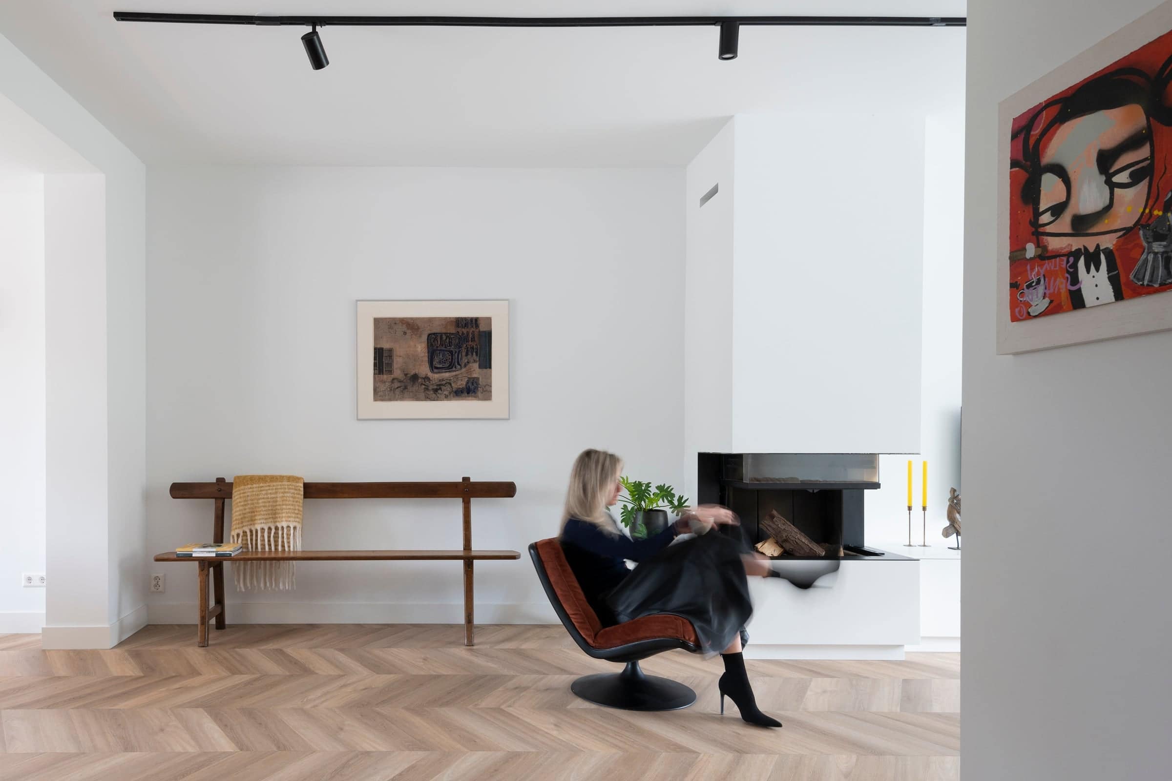 Lichte woonkamer met een visgraat houten vloer, witte haard en een terracotta fauteuil in een woning in Noord-Brabant