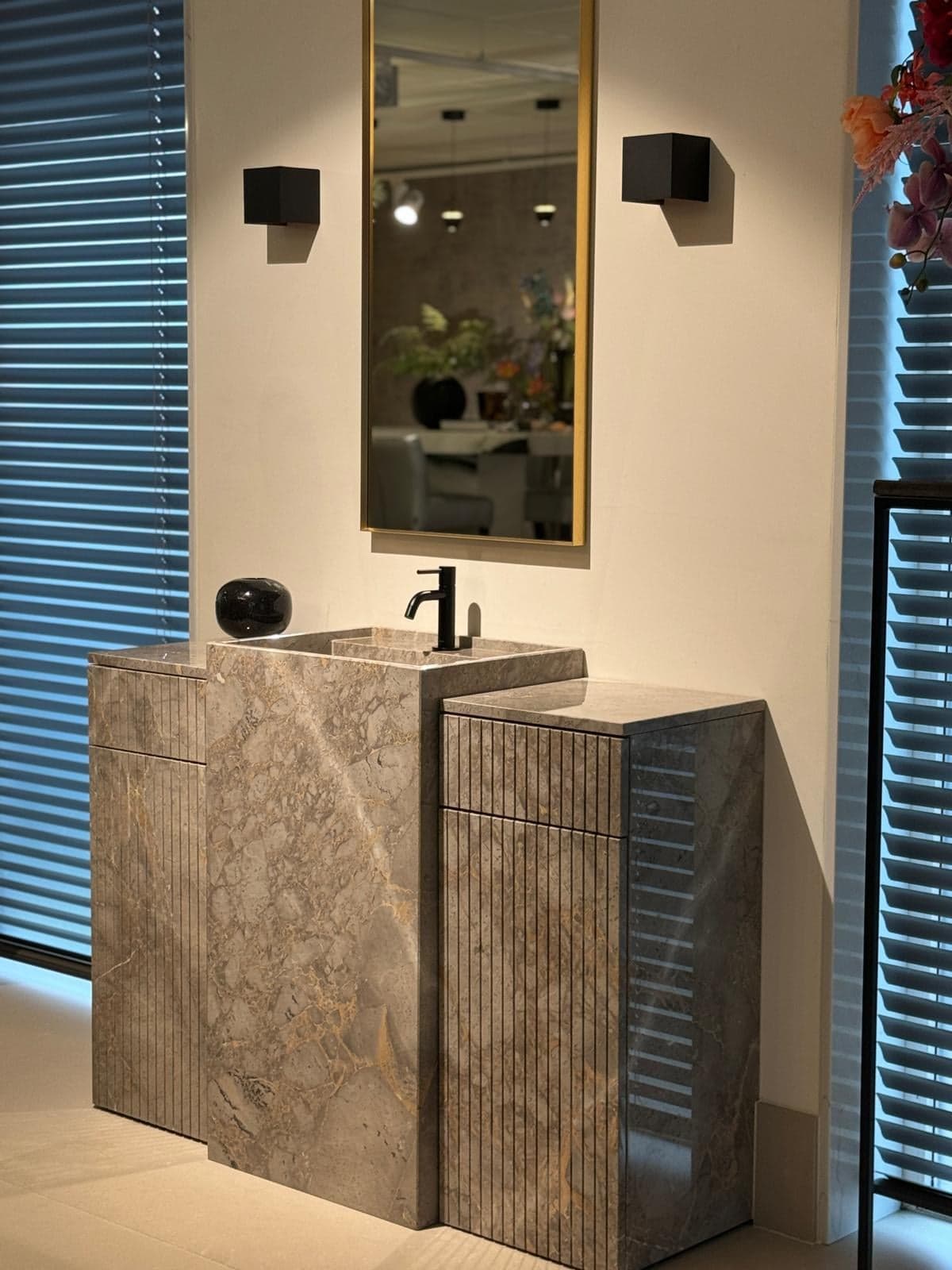 Natuurstenen wastafelmeubel met een spiegel en wandlampen in een natuursteen-showroom in Tilburg