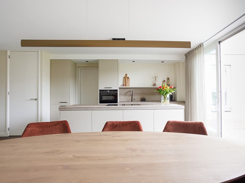 Eettafel van licht eikenhout met zicht op de open keuken in een gerenoveerd woonhuis in Oisterwijk